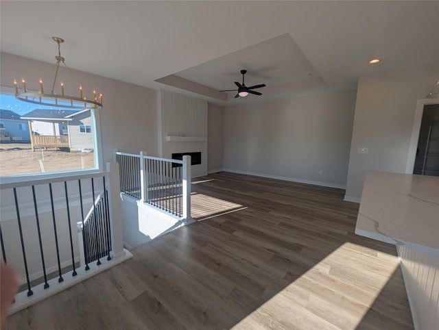 interior space with dark hardwood / wood-style flooring, a large fireplace, ceiling fan with notable chandelier, and a raised ceiling