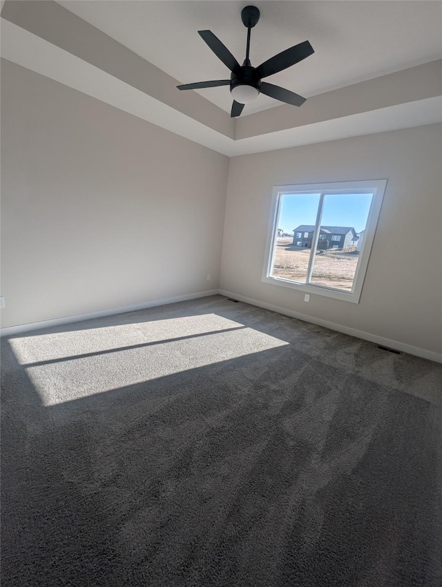 carpeted empty room with ceiling fan and a raised ceiling