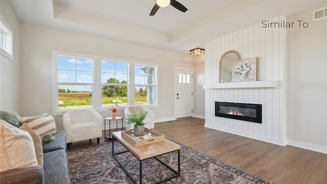 living room featuring ceiling fan, a fireplace, dark hardwood / wood-style flooring, and a raised ceiling