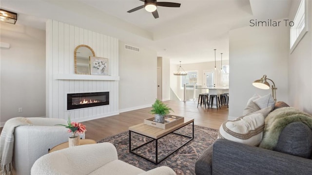 living room featuring ceiling fan, wood-type flooring, a fireplace, and a tray ceiling