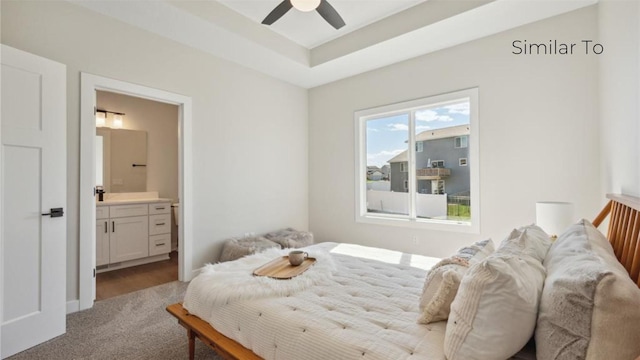 bedroom featuring a raised ceiling, connected bathroom, light colored carpet, and ceiling fan