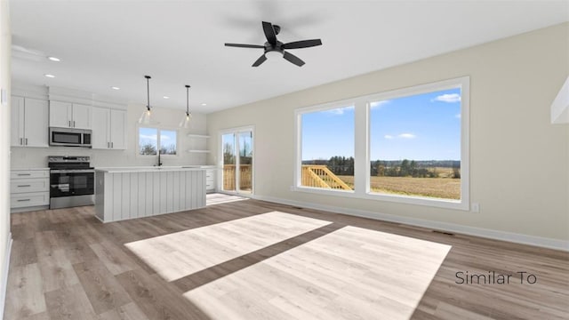 kitchen featuring appliances with stainless steel finishes, decorative light fixtures, white cabinets, a center island, and light hardwood / wood-style flooring