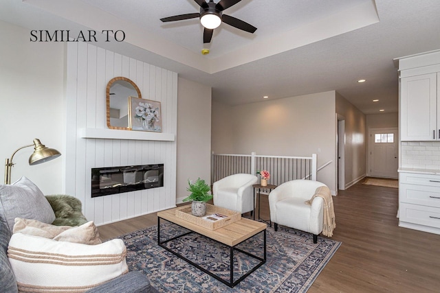 living room with a raised ceiling, ceiling fan, dark hardwood / wood-style floors, and a fireplace