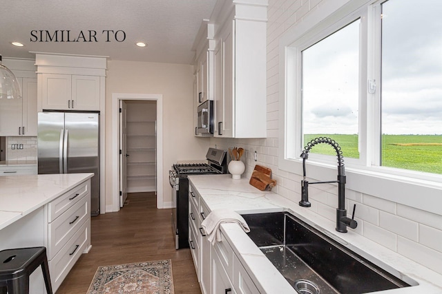 kitchen featuring sink, white cabinets, decorative backsplash, stainless steel appliances, and light stone countertops