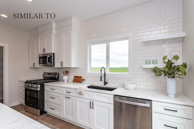 kitchen with stainless steel appliances, sink, white cabinets, and light stone counters