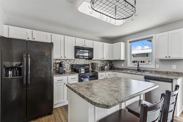 kitchen with a kitchen island, white cabinetry, sink, a kitchen bar, and black appliances