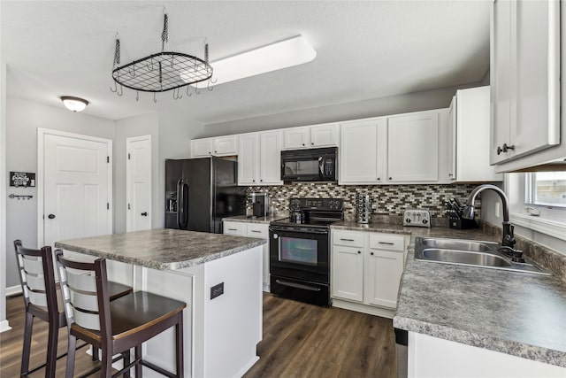 kitchen featuring white cabinetry, sink, a kitchen breakfast bar, a center island, and black appliances