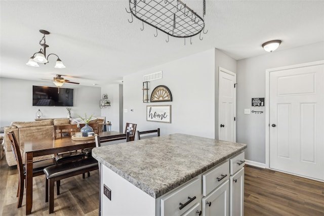 kitchen featuring pendant lighting, ceiling fan, a textured ceiling, a kitchen island, and dark hardwood / wood-style flooring