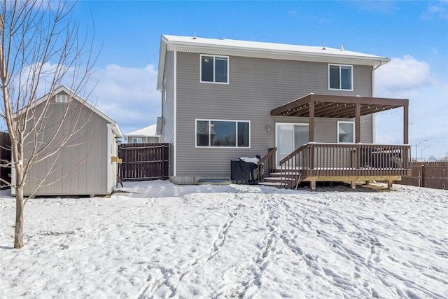 snow covered back of property with a deck and a shed