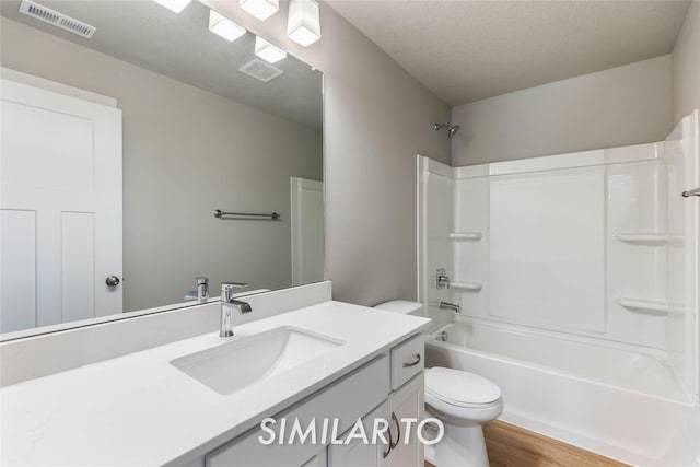 full bathroom with shower / bathing tub combination, hardwood / wood-style flooring, vanity, toilet, and a textured ceiling