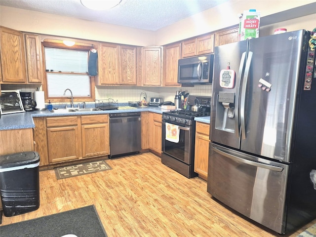 kitchen with sink, backsplash, stainless steel appliances, a textured ceiling, and light wood-type flooring