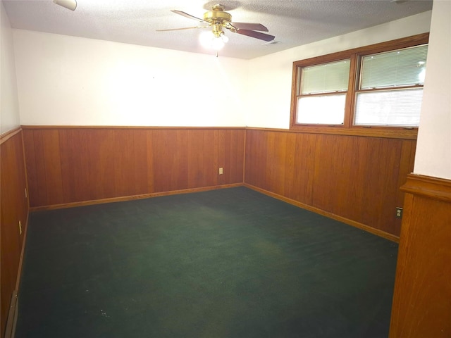 carpeted spare room featuring ceiling fan, wooden walls, and a textured ceiling