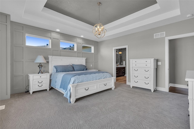 carpeted bedroom featuring ensuite bath, a raised ceiling, and a notable chandelier