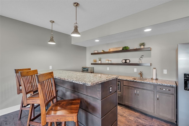 kitchen with dark hardwood / wood-style floors, a breakfast bar area, light stone counters, and kitchen peninsula