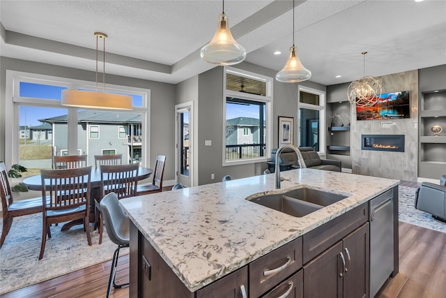 kitchen with sink, dark wood-type flooring, dark brown cabinetry, a center island with sink, and stainless steel dishwasher