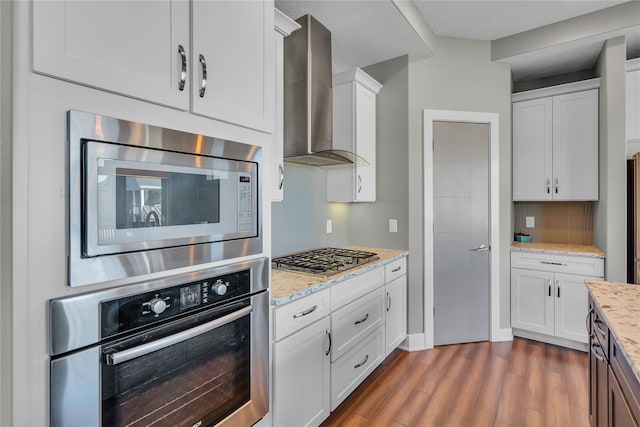 kitchen with stainless steel appliances, dark hardwood / wood-style floors, light stone counters, white cabinets, and wall chimney exhaust hood