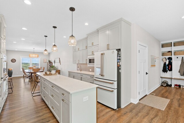 kitchen with stainless steel microwave, decorative light fixtures, white cabinetry, a center island, and white fridge with ice dispenser