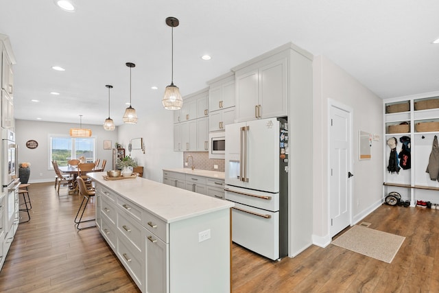 kitchen featuring white appliances, wood finished floors, a center island, backsplash, and recessed lighting