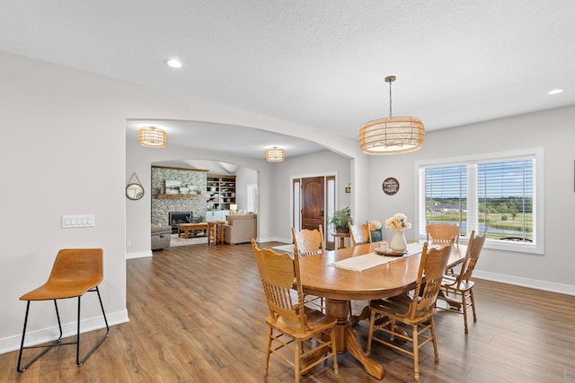 dining space featuring arched walkways, recessed lighting, a fireplace, wood finished floors, and baseboards