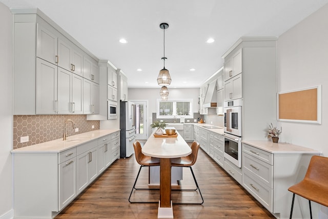 kitchen with dark wood-style flooring, black electric cooktop, light countertops, wall chimney range hood, and a sink