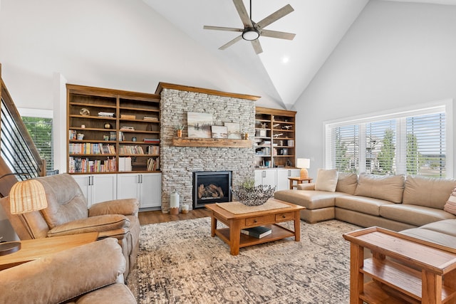 living room featuring ceiling fan, high vaulted ceiling, wood finished floors, and a stone fireplace