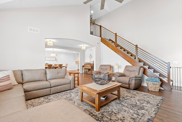 living room with visible vents, arched walkways, wood finished floors, stairs, and high vaulted ceiling