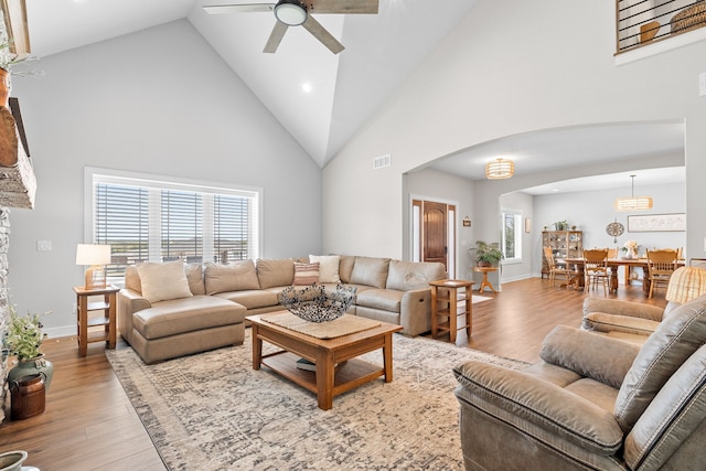 living room with arched walkways, high vaulted ceiling, and wood finished floors