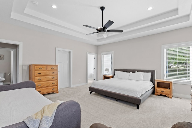 bedroom featuring a raised ceiling, light carpet, ensuite bath, and baseboards