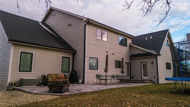 rear view of property featuring a patio area, an outdoor fire pit, a trampoline, and a lawn