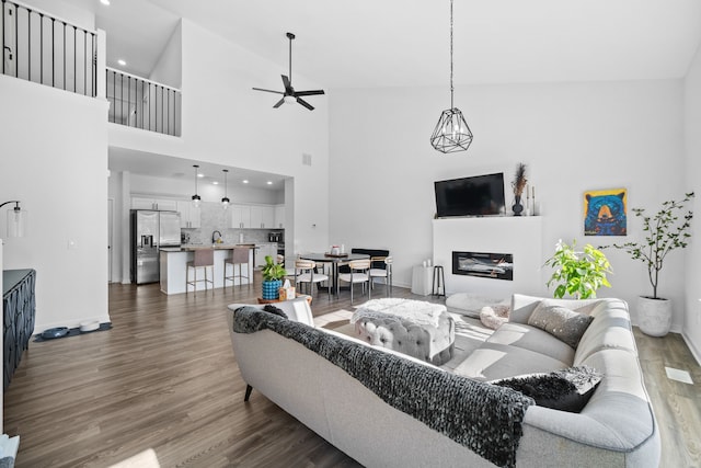 living room featuring dark wood-type flooring, ceiling fan, and a towering ceiling