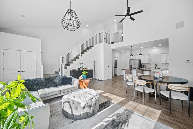 living room featuring wood-type flooring, sink, a towering ceiling, and ceiling fan with notable chandelier