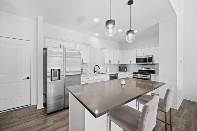 kitchen with a kitchen bar, white cabinetry, a center island, hanging light fixtures, and stainless steel appliances