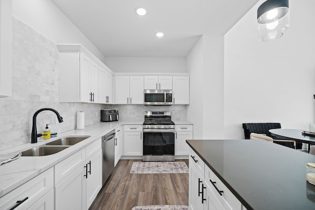 kitchen featuring dark wood finished floors, decorative backsplash, appliances with stainless steel finishes, white cabinetry, and a sink