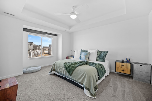 carpeted bedroom featuring a raised ceiling, baseboards, visible vents, and ceiling fan