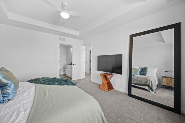 carpeted bedroom featuring a raised ceiling, ceiling fan, and ensuite bath