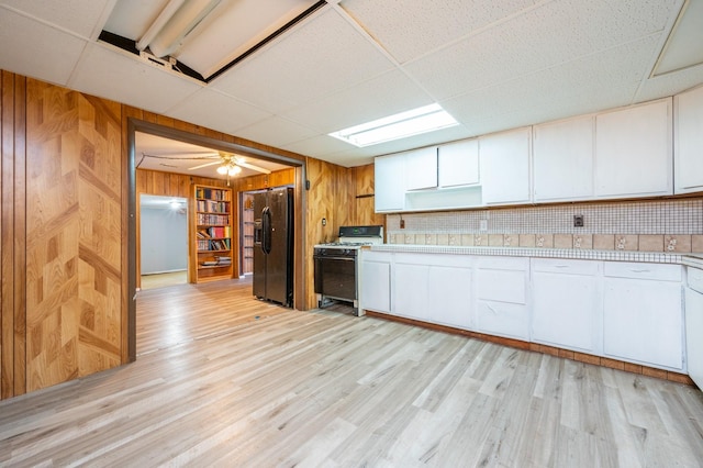 kitchen featuring light hardwood / wood-style flooring, black refrigerator with ice dispenser, white range with gas stovetop, and white cabinets