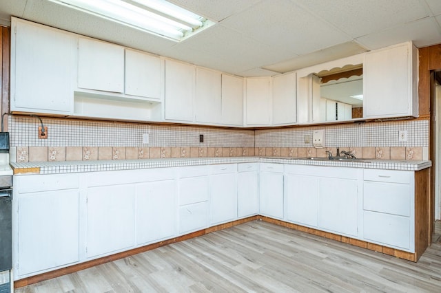 kitchen with white cabinetry, sink, decorative backsplash, a drop ceiling, and light wood-type flooring