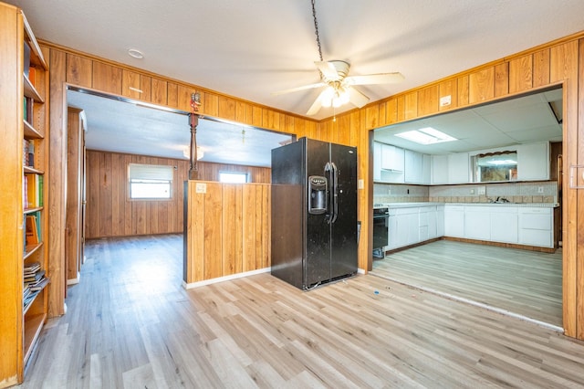 kitchen with black fridge, sink, light hardwood / wood-style floors, and wood walls