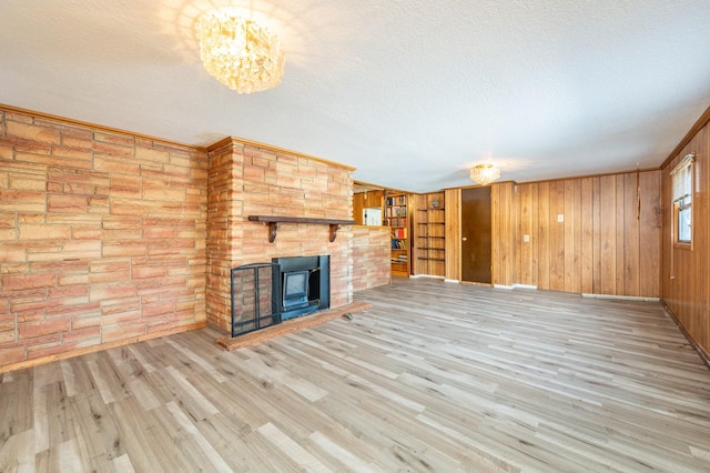 unfurnished living room with wooden walls, a brick fireplace, a textured ceiling, and light wood-type flooring