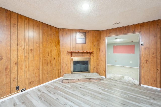 unfurnished living room featuring wooden walls, light hardwood / wood-style floors, and a textured ceiling