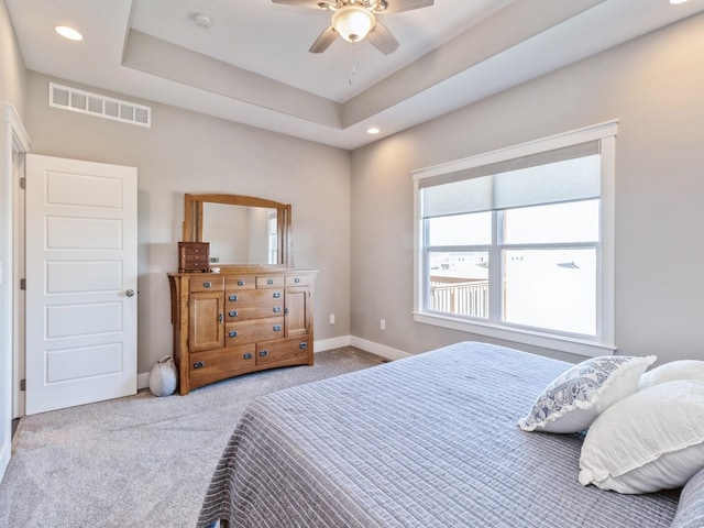 bedroom featuring ceiling fan, a tray ceiling, and light carpet