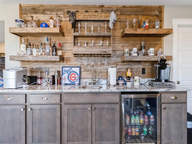 bar with wine cooler, dark brown cabinetry, and light stone countertops