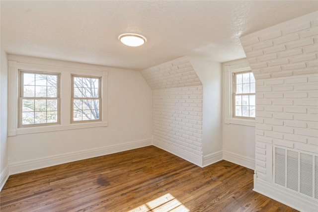 additional living space with brick wall, dark wood-type flooring, a textured ceiling, and vaulted ceiling