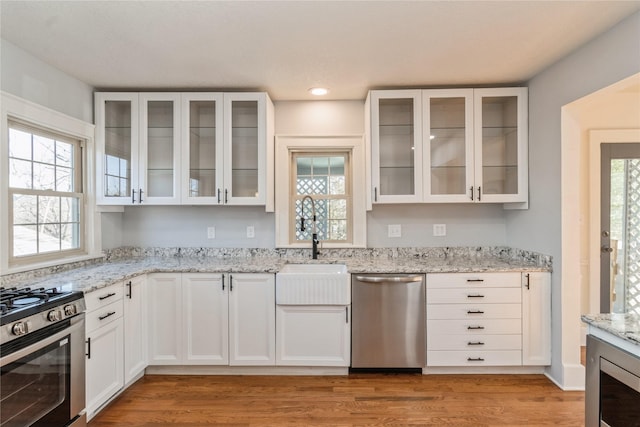 kitchen featuring light hardwood / wood-style flooring, appliances with stainless steel finishes, white cabinetry, light stone counters, and wine cooler