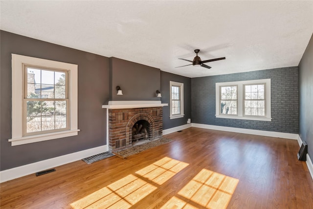 unfurnished living room featuring hardwood / wood-style flooring, a brick fireplace, a textured ceiling, and ceiling fan