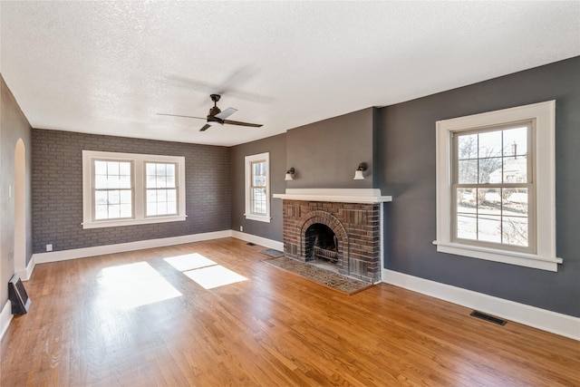 unfurnished living room with a textured ceiling, hardwood / wood-style flooring, ceiling fan, brick wall, and a fireplace