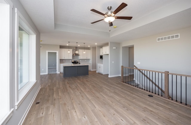 unfurnished living room with a tray ceiling, light hardwood / wood-style flooring, and ceiling fan