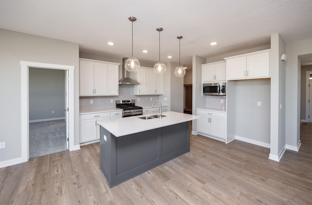 kitchen with sink, wall chimney range hood, appliances with stainless steel finishes, an island with sink, and white cabinets