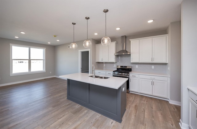 kitchen featuring white cabinets, stainless steel range with gas cooktop, sink, and wall chimney range hood