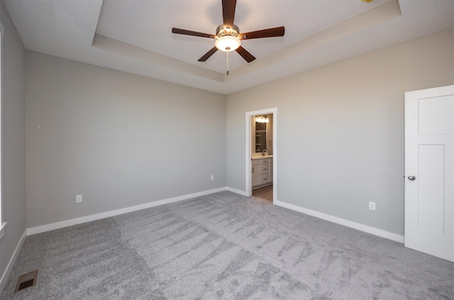 carpeted spare room featuring a raised ceiling and ceiling fan